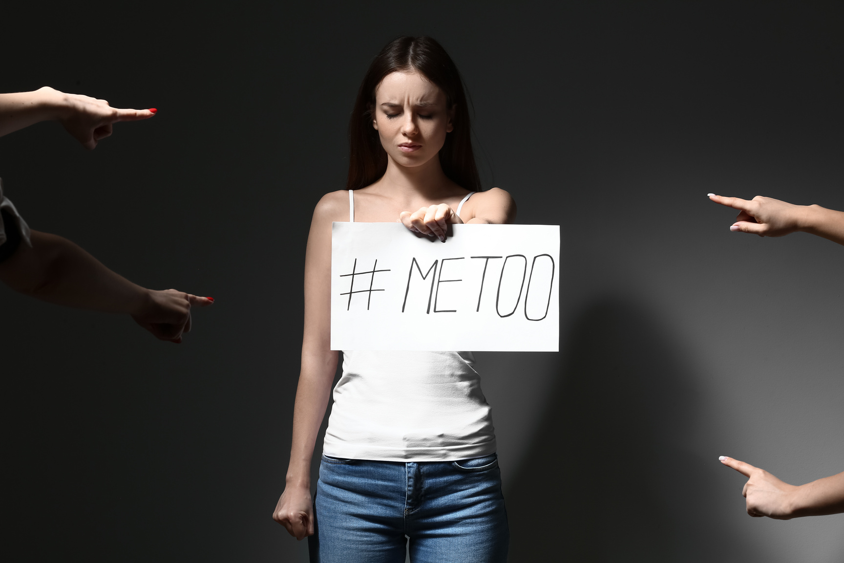 People Pointing at Young Woman Who Is Holding Paper with Hashtag MeToo on Dark Background
