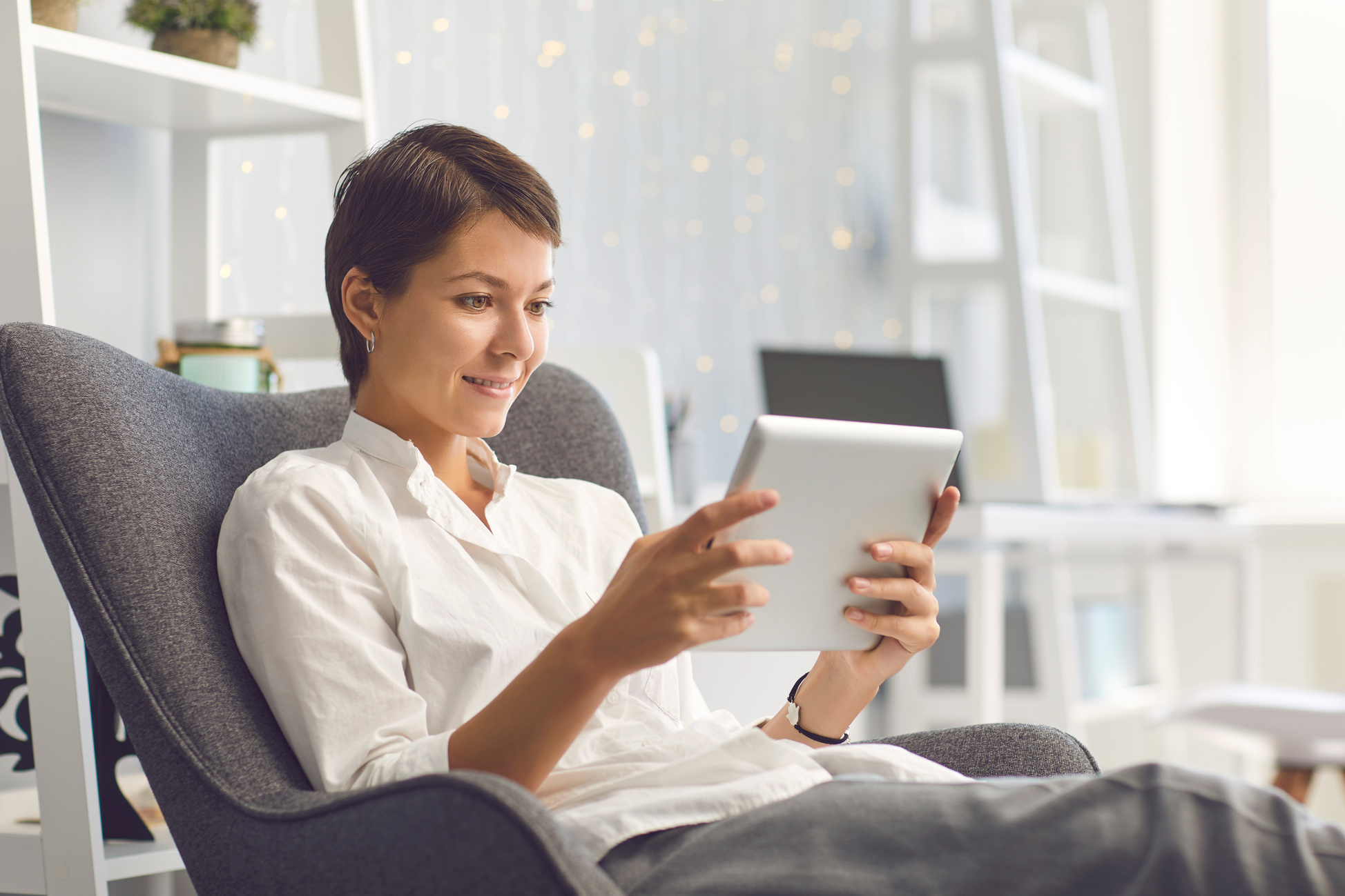 Happy Lady Watching Videos on Tablet Sitting in Cozy Armchair in the Living Room